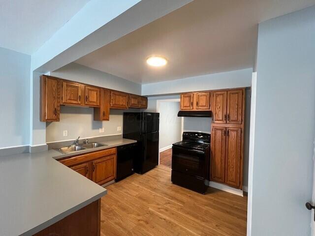 kitchen featuring black appliances, a sink, under cabinet range hood, and brown cabinetry