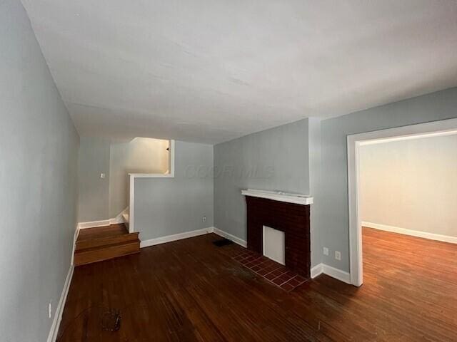 unfurnished living room with wood finished floors, baseboards, and stairs