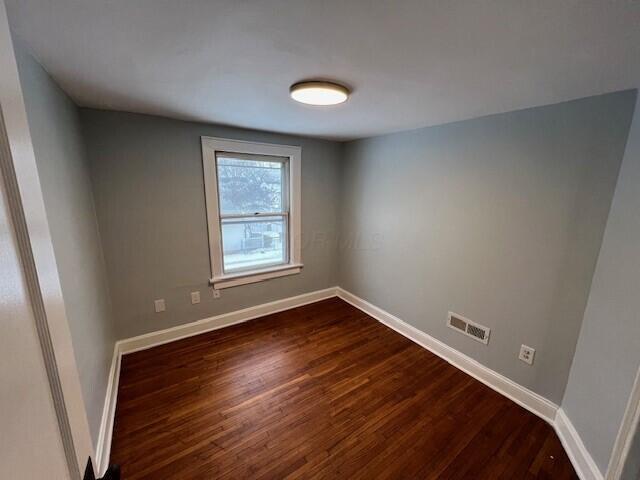 empty room with dark wood-type flooring and baseboards