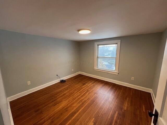 spare room featuring baseboards and dark wood-type flooring