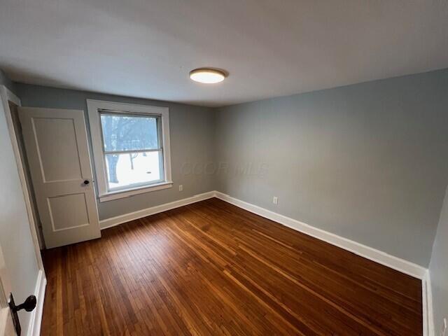 spare room with baseboards and dark wood-style floors