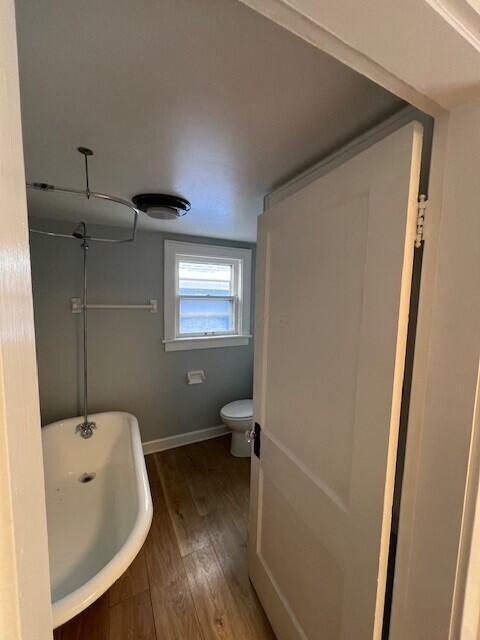 full bathroom with a freestanding tub, wood finished floors, toilet, and baseboards