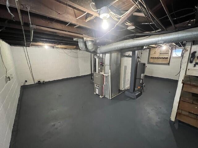 basement with gas water heater, heating unit, and concrete block wall