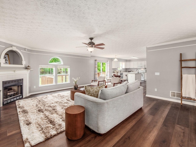living area with ceiling fan, dark wood-type flooring, a tile fireplace, a textured ceiling, and baseboards
