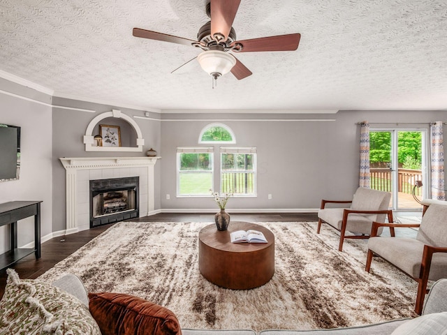 living room featuring wood finished floors, a textured ceiling, a tiled fireplace, ceiling fan, and baseboards