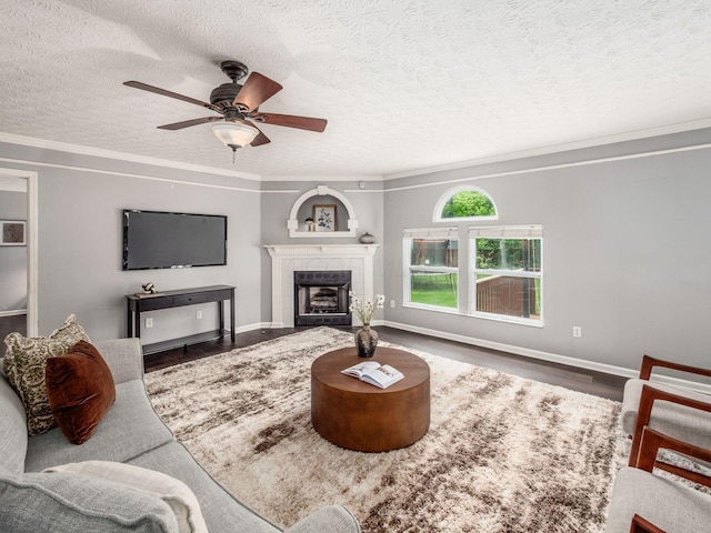 living room featuring wood finished floors, a tiled fireplace, ceiling fan, a textured ceiling, and crown molding