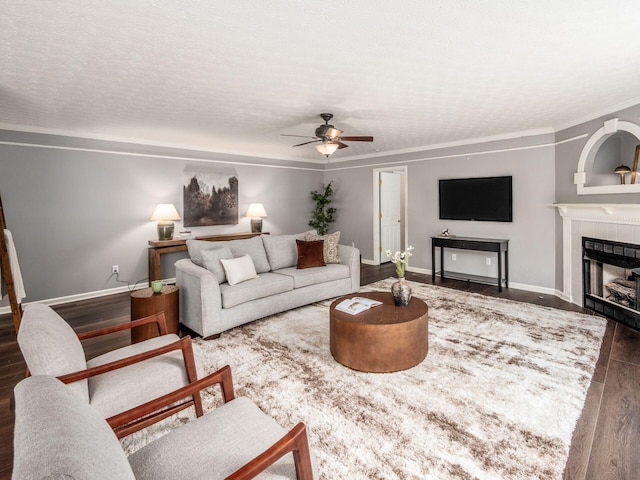 living room with wood finished floors, ceiling fan, baseboards, ornamental molding, and a fireplace