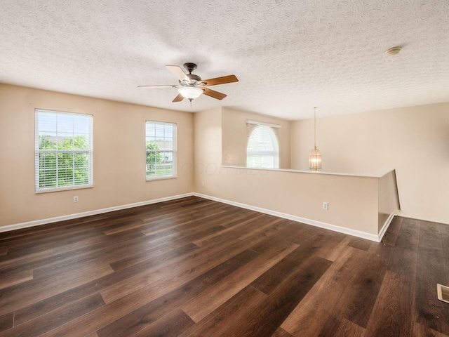 unfurnished room featuring healthy amount of natural light, dark wood finished floors, a ceiling fan, baseboards, and a textured ceiling
