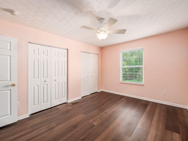 unfurnished bedroom featuring multiple closets, dark wood-style floors, baseboards, a textured ceiling, and ceiling fan