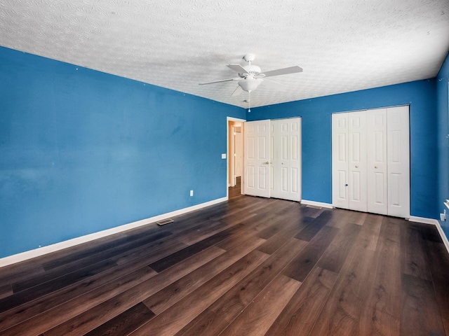 unfurnished bedroom with wood finished floors, baseboards, multiple closets, a ceiling fan, and a textured ceiling