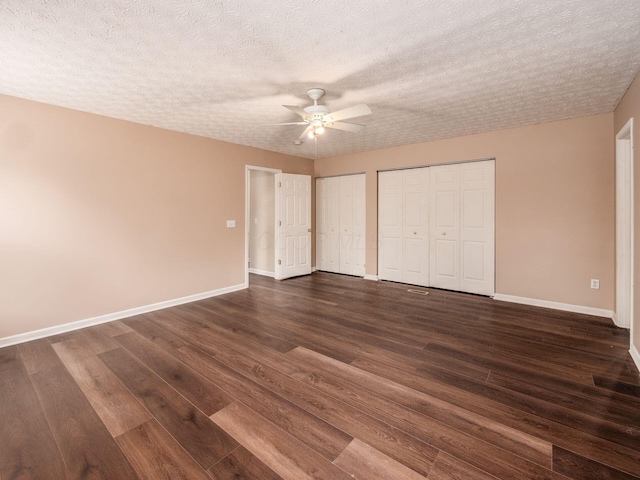 unfurnished bedroom featuring multiple closets, dark wood-type flooring, baseboards, a textured ceiling, and a ceiling fan
