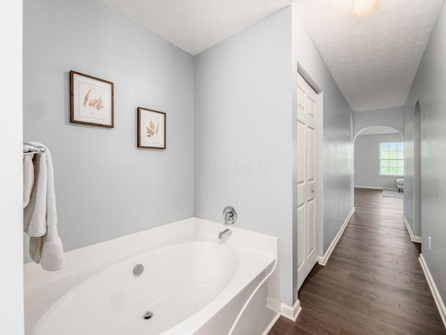 full bath featuring a bath, a textured ceiling, wood finished floors, and baseboards