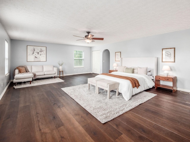 bedroom with arched walkways, a textured ceiling, baseboards, dark wood-style floors, and ceiling fan