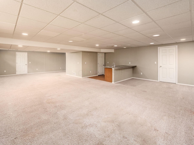 finished below grade area featuring carpet floors, a drop ceiling, baseboards, recessed lighting, and wet bar