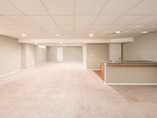 finished below grade area with carpet, a drop ceiling, recessed lighting, baseboards, and a sink