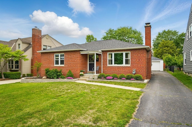 view of front facade featuring brick siding, a front yard, a garage, an outbuilding, and a chimney