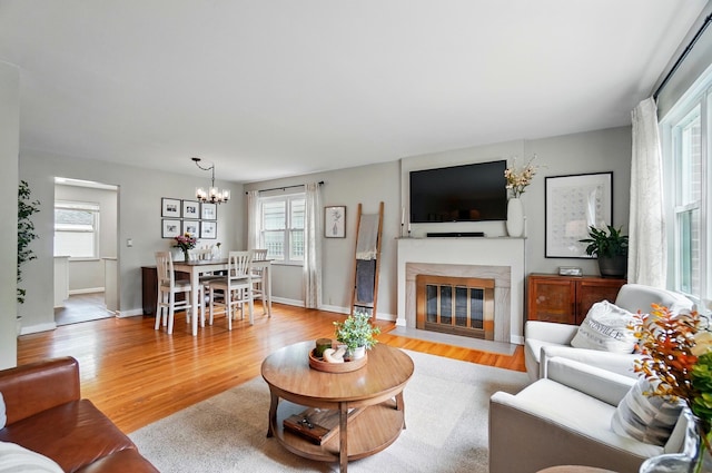living area with a chandelier, light wood-type flooring, a premium fireplace, and baseboards