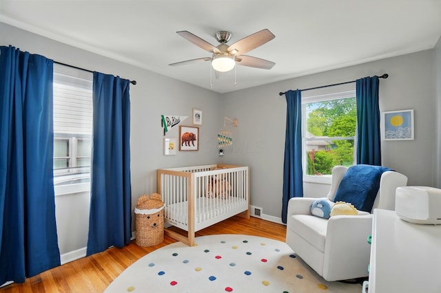 bedroom with a nursery area, wood finished floors, a ceiling fan, and baseboards