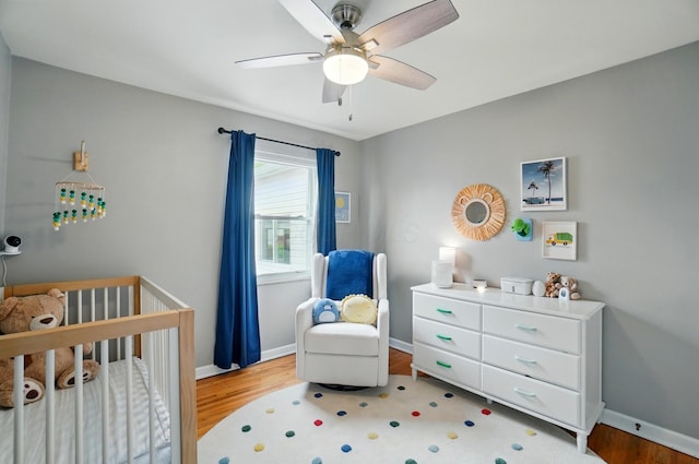 bedroom featuring a nursery area, wood finished floors, baseboards, and a ceiling fan