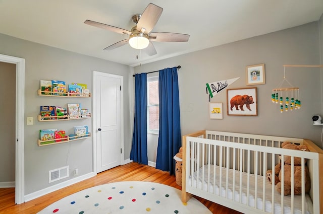 bedroom with wood finished floors, a nursery area, baseboards, and ceiling fan