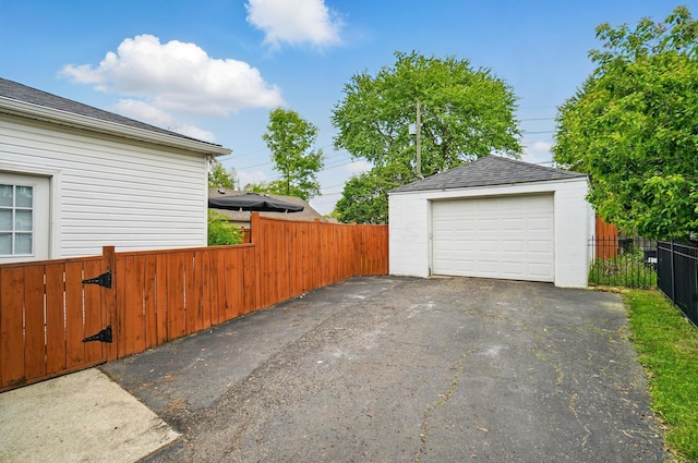 detached garage featuring asphalt driveway and fence