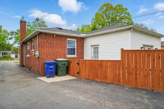 view of home's exterior featuring fence, a chimney, a shingled roof, and brick siding