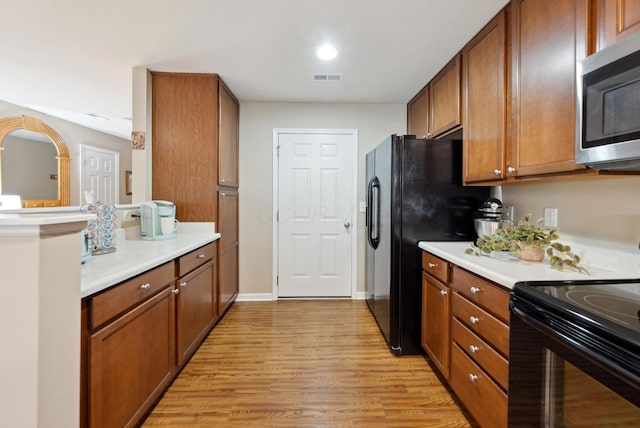 kitchen with black appliances, light wood-style floors, light countertops, and brown cabinets