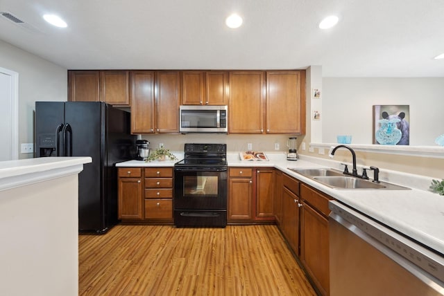kitchen with black appliances, a sink, brown cabinetry, light wood-style flooring, and recessed lighting