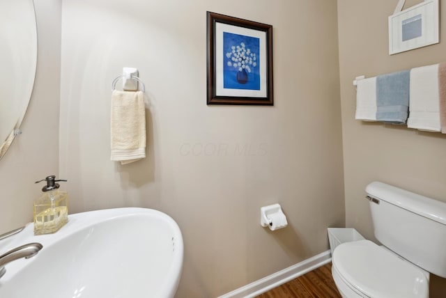 half bathroom featuring toilet, wood finished floors, baseboards, and a sink