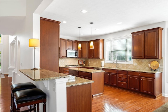6415 Green Stone Loop, Dublin, OH 43016 - kitchen with appliances with stainless steel finishes, a center island, a sink, light wood-style floors, and light stone counters