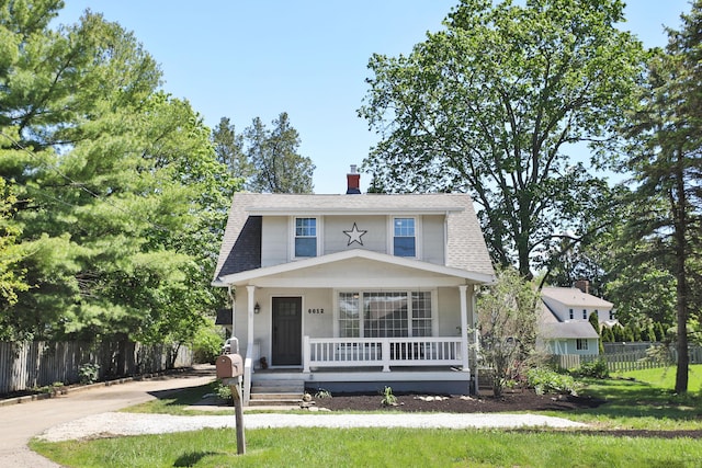 colonial inspired home with a porch, roof with shingles, and a chimney