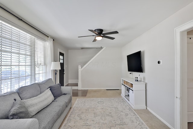 living room featuring a ceiling fan, baseboards, light colored carpet, and stairway
