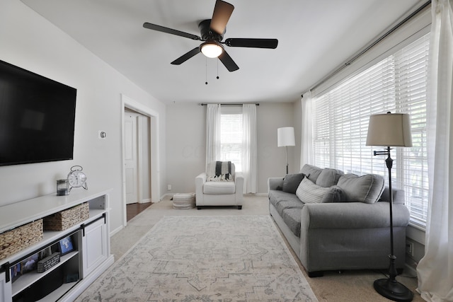 living area with light colored carpet, a ceiling fan, and baseboards