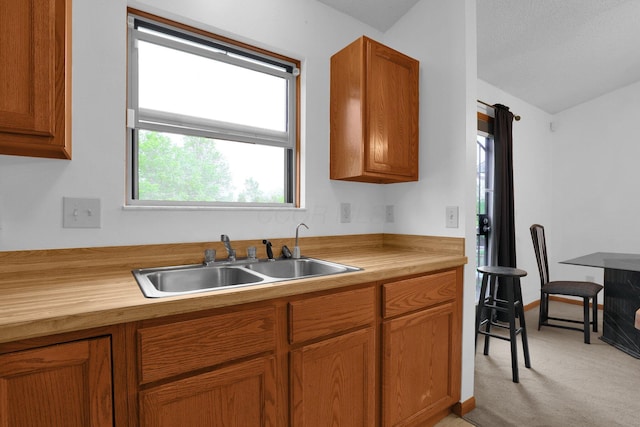 kitchen featuring a sink, light colored carpet, butcher block counters, brown cabinetry, and lofted ceiling