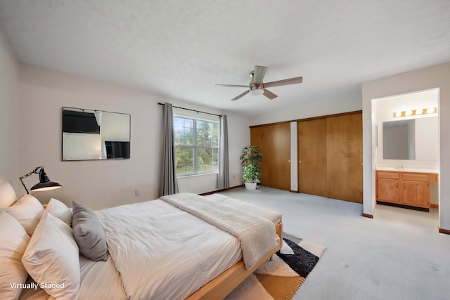 bedroom featuring light carpet, a closet, ensuite bath, ceiling fan, and baseboards