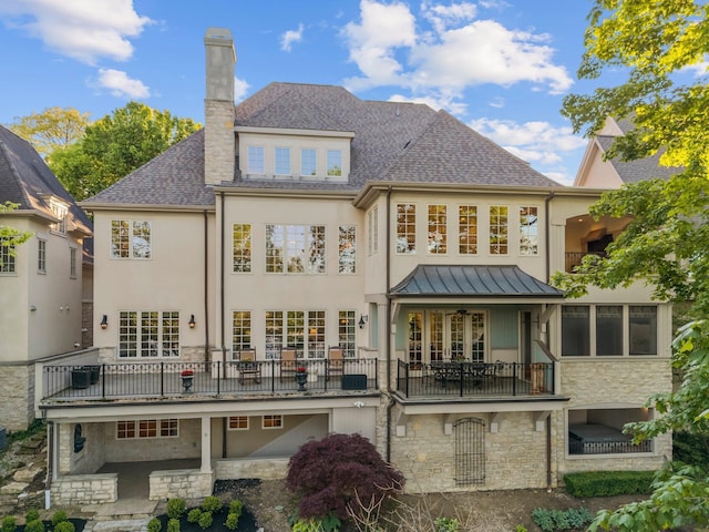 back of house with a balcony, stone siding, a standing seam roof, a chimney, and stucco siding