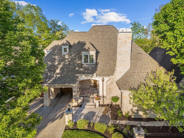 view of front of house with stone siding, a shingled roof, a chimney, and a patio