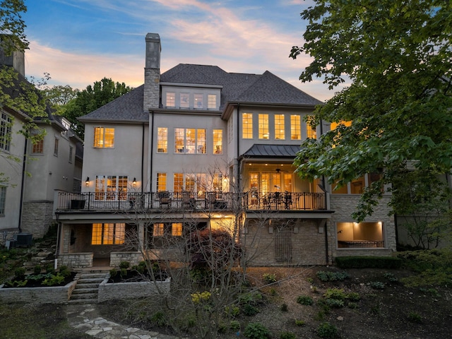 rear view of property with a balcony, stone siding, a chimney, and stucco siding