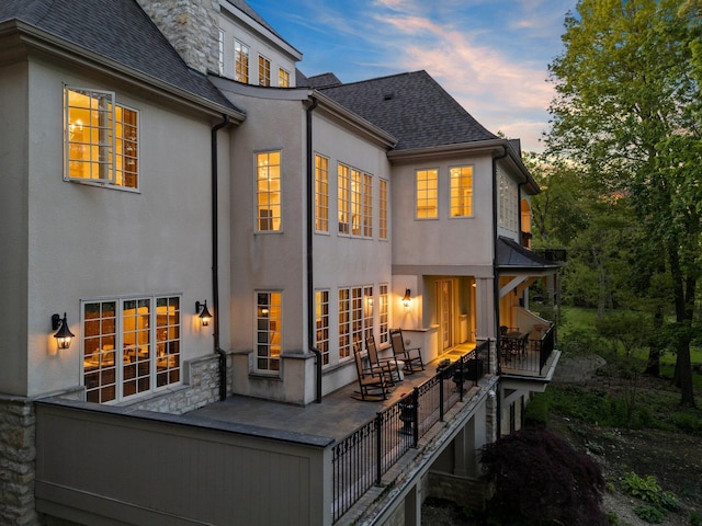 rear view of house featuring stucco siding, stone siding, and a shingled roof
