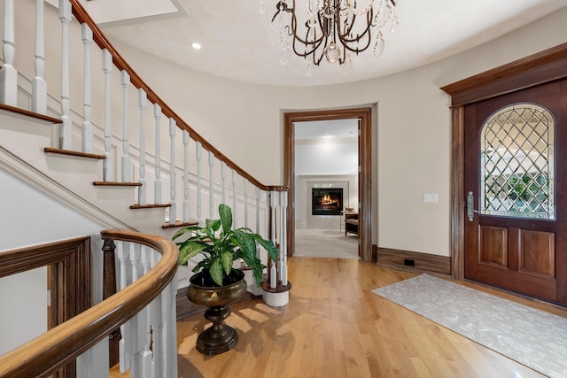 entryway with stairs, wood finished floors, a chandelier, recessed lighting, and a glass covered fireplace