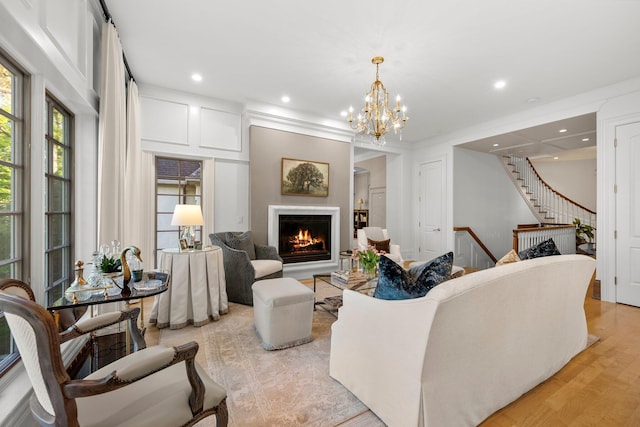 living area featuring a warm lit fireplace, stairs, recessed lighting, a chandelier, and light wood-style floors