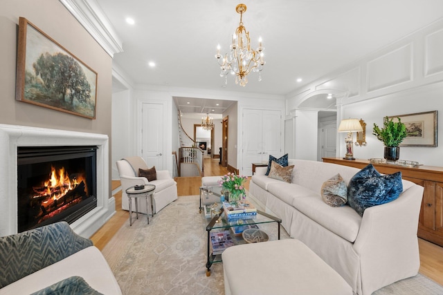 living area featuring a chandelier, light wood-type flooring, arched walkways, recessed lighting, and a lit fireplace