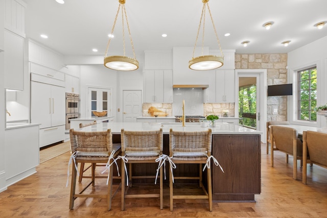kitchen featuring a kitchen island with sink, paneled refrigerator, double oven, light countertops, and white cabinets