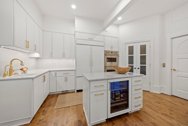 kitchen with beverage cooler, a sink, light wood-style flooring, double oven, and recessed lighting