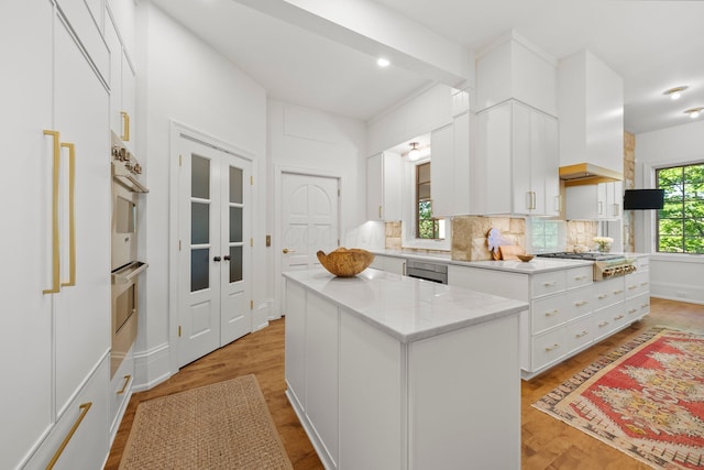 kitchen featuring appliances with stainless steel finishes, backsplash, white cabinetry, light wood-style floors, and a center island