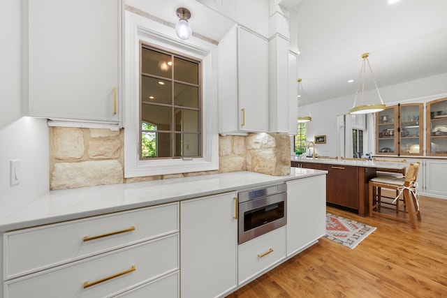 kitchen featuring glass insert cabinets, decorative backsplash, a sink, light wood-type flooring, and white cabinets