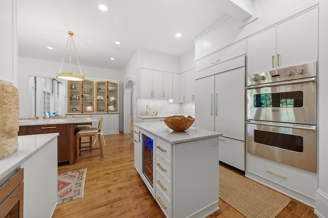 kitchen featuring built in appliances, a center island, decorative backsplash, white cabinetry, and glass insert cabinets