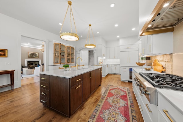 kitchen with stainless steel gas stovetop, custom exhaust hood, a sink, white cabinets, and dark brown cabinetry
