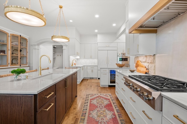kitchen featuring stainless steel appliances, a sink, white cabinets, light wood finished floors, and custom exhaust hood