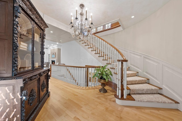 stairs featuring a decorative wall, a chandelier, wood finished floors, wainscoting, and recessed lighting